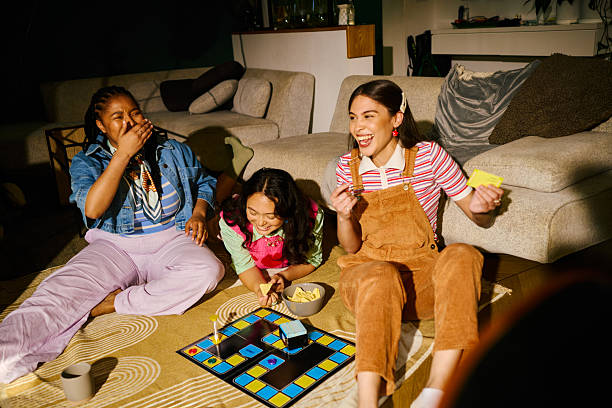 Group of diverse young adult women enjoying board game night, laughing, eating snacks and having fun