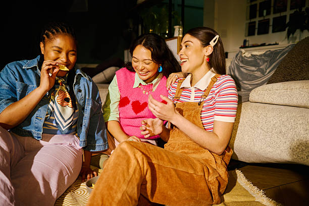 Three young adult women enjoying an offline friendship moment, sharing smiles and snacks indoors