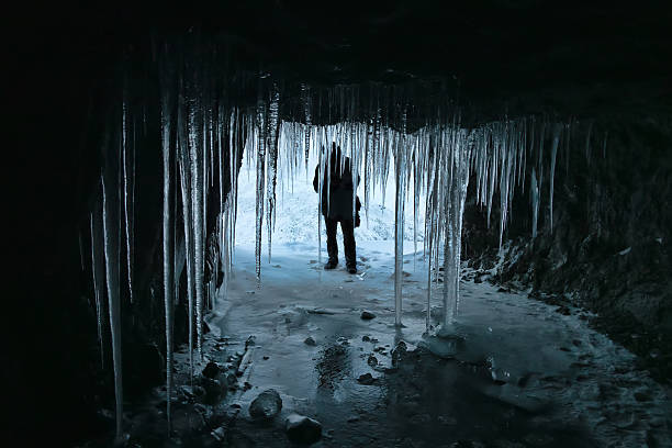 The entrance to the ice cave is hung with large icicles. Spelunker in the background