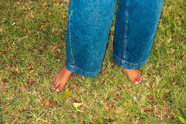 Person standing barefoot in jeans on green grass, connecting with nature