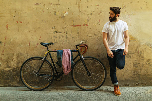 Casual bearded man leaning against a textured urban wall with a vintage bicycle in Florence, Italy, representing city lifestyle, urban mobility, and relaxed contemporary travel atmosphere.