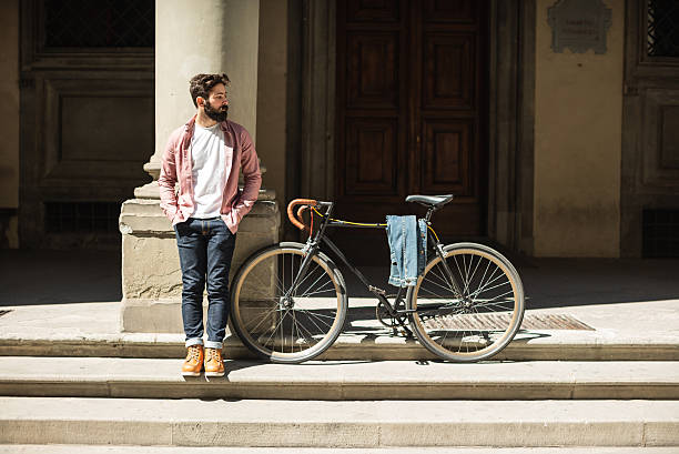 Young man standing on the steps of a historic building, with a bicycle beside him, conveying urban lifestyle, slow travel in a classic architectural setting.