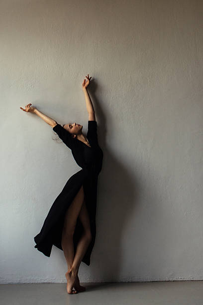 istock Graceful dancer in black dress leans against a pale wall in a dramatic studio pose 2255225196