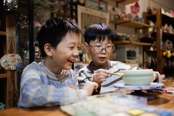 Boy shaping clay with his hands while another child uses a toy pottery wheel. A calm and creative moment at home, ideal for educational or parenting visuals.