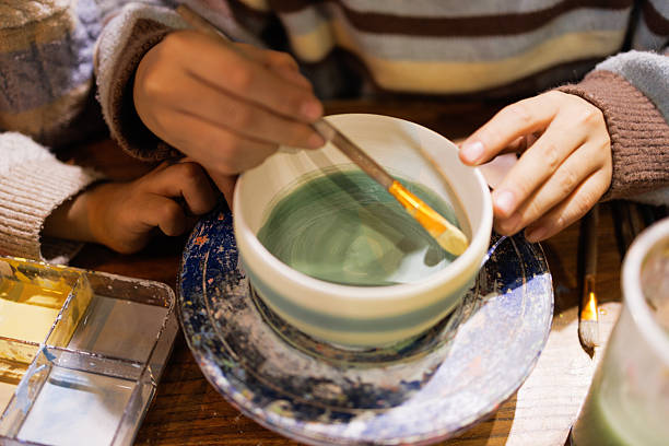 These are two little Asian Boys, about 10 years old. They are brothers, dressed in casual clothes, and are coloring their pottery bowls in a handicraft workshop. They are very happy and serious.