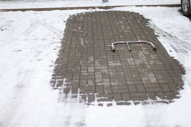 Compact parking spot, Compact parking space with metal hinge and snow rim in shade, Parking barrier folded on cleared surface with snow and brick outline in cool lighting