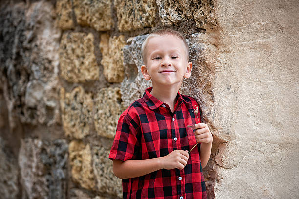 Smiling Young Boy in Red Plaid Shirt by Stone Wall