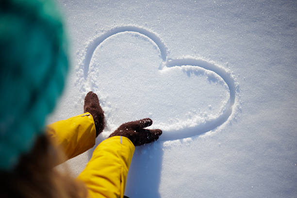 Gloved hands drawing a heart in fresh snow for winter love concept background with copy space