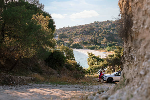 Mid-30s couple leans on their parked car, enjoying the view of the ocean. Romantic and peaceful lifestyle moment at a hidden beach.