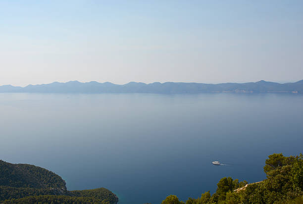 A breathtaking high angle view from the Sveti Ivan peak on Peljesac peninsula overlooking the blue Adriatic Sea towards the distant silhouette of Mljet Island under a hazy sky
