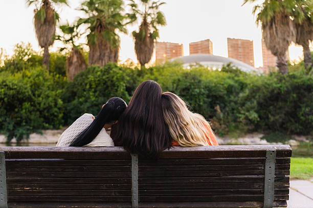 Three friends sitting closely on a park bench, enjoying a moment of togetherness