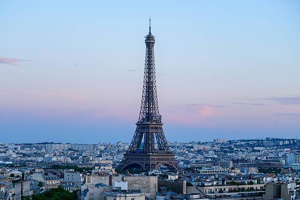 Iconic Eiffel Tower stands tall above the Paris skyline, framed by soft pastel hues and scattered clouds at dusk, with city rooftops stretching into the distance.