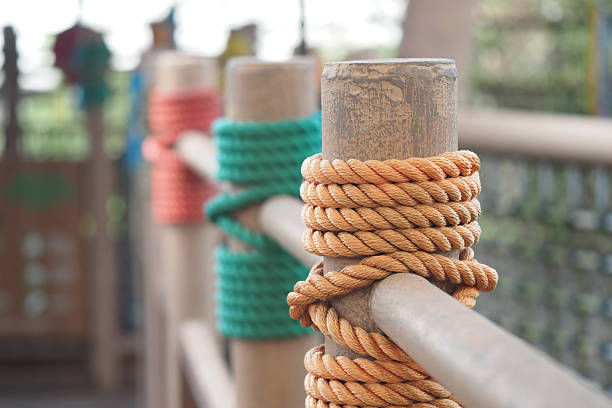 Colorful ropes are tightly wound around wooden posts in a park.