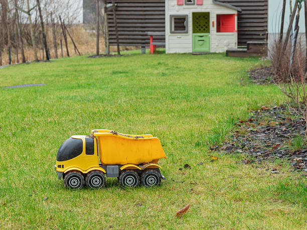 A bright yellow toy construction vehicle, resembling a front-end loader with large black wheels and a functional scoop, sits on a green grass lawn for outdoor play