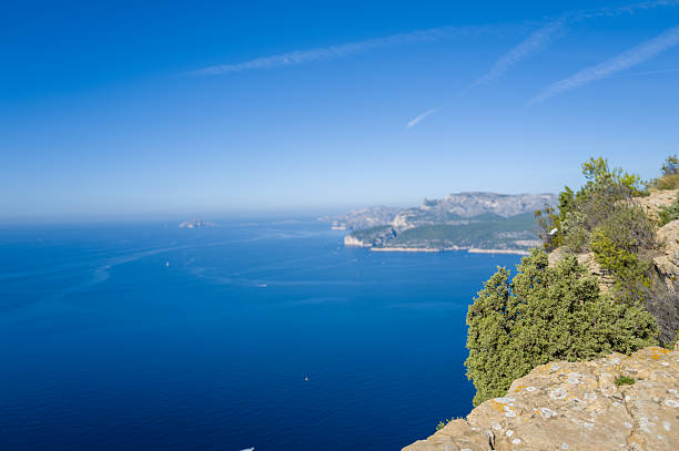 A reddish-brown rock partially submerged in the turquoise-blue waters of Konyaaltı Beach in Antalya, Turkey. The calm sea surface features gentle ripples, and sunlight from above casts a soft shadow beneath the rock. The vibrant contrast between the earthy tones and clear water creates a peaceful and visually striking coastal scene. This image is suitable for travel and nature content, beach resort promotions, wellness blogs, vacation brochures, and materials related to Mediterranean landscapes or seaside relaxation.