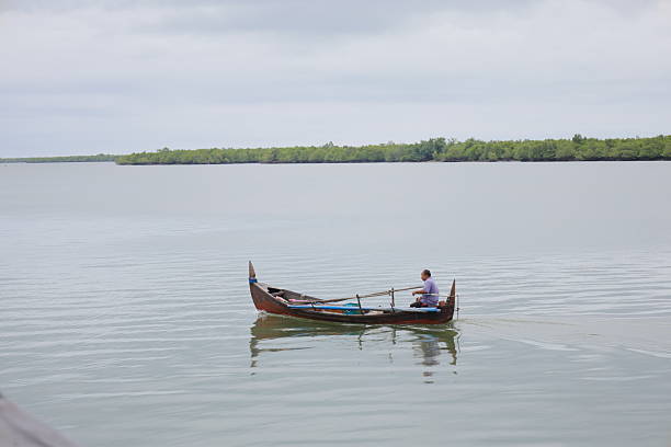 A fisherman sits on a traditional wooden boat while crossing calm waters in Kuala Langsa, Langsa City, Aceh Province, Indonesia, on December 16, 2025. The area is known for its coastal and mangrove ecosystems that support local fishing activities.