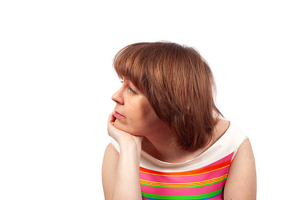 A sad woman has a pensive and troubled expression while resting her chin on her hand.
