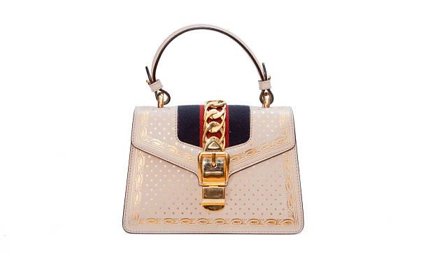 A luxury beige leather top handle handbag featuring elegant gold chain hardware, decorative embossed pattern, structured silhouette and classic flap closure photographed isolated on a white background for fashion, retail, branding and e commerce use