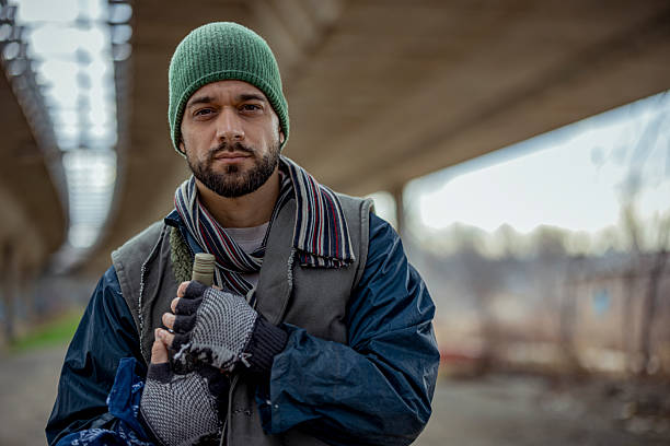 istock Homeless Man Holding Bottle Looking at Camera Under City Bridge 2255269076