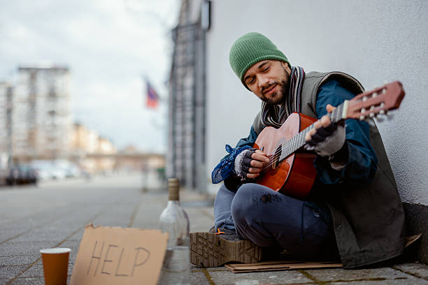 istock Homeless Man Sitting on Pavement Playing Guitar in Cold Weather 2255269079