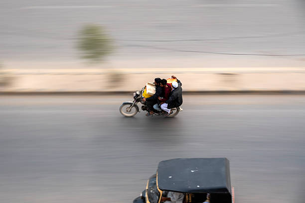 Karachi, Pakistan - December 18, 2025: High-angle motion blur photograph of young men riding motorcycles on an urban road. Captured from above