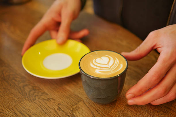 Hands carefully position a latte cup with intricate design on a table.