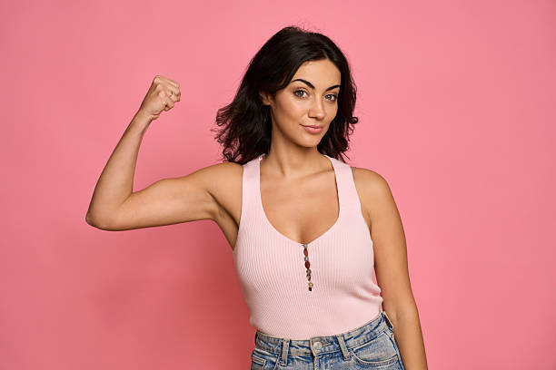 Woman standing against a pink background flexing her bicep, showing power
