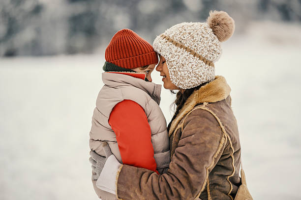 Mother and son sharing a tender moment, forehead to forehead, while embracing outdoors during a cold winter day, showcasing their strong familial bond and love