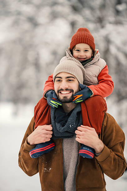 Happy father giving his young son a piggyback ride on his shoulders outdoors, enjoying a fun winter day together in the snowy landscape, bonding and creating joyful family memories
