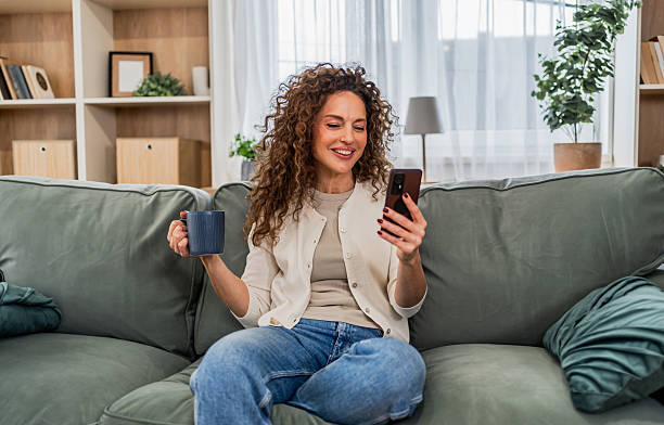 istock Smiling woman relaxing on sofa using smartphone 2255284302