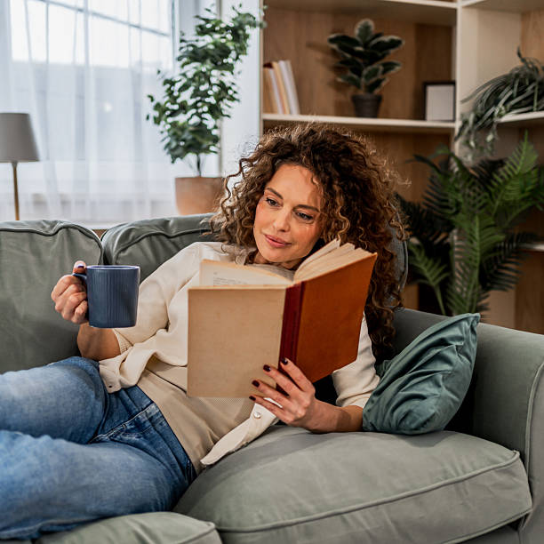 istock Woman relaxing on sofa reading book and drinking coffee 2255284650