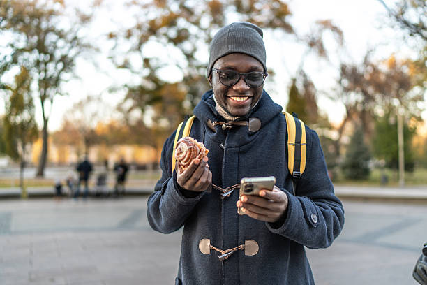 istock Young man using phone and eating pastry outdoors 2255287079