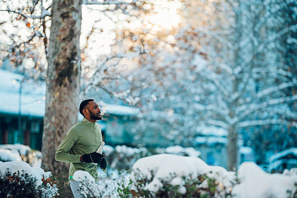 Man in his 30s jogging through a snowy park, focused winter training amid frost-covered trees and cold fresh air