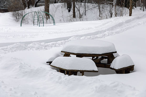 Picnic table covered with snow in park with playground in winter season. Snowy day.