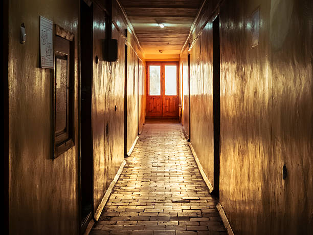 Long, narrow corridor featuring warm light reflecting off wooden walls and a brick floor, leading towards a bright exit door, conveying concepts of passage, hope, and transition
