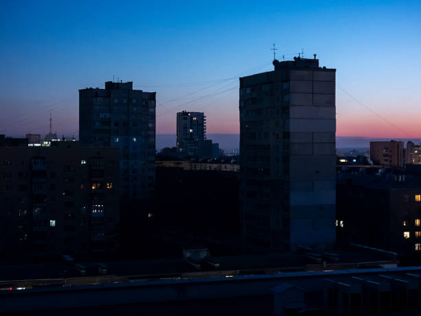 Urban residential buildings standing against a twilight sky, showcasing the transition from day to night in an older cityscape with distant lights illuminating the horizon