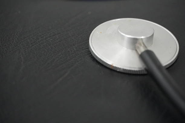 The polished silver diaphragm of a stethoscope is meticulously captured in a tight close-up, lying on a dark, textured background, symbolizing medical precision.