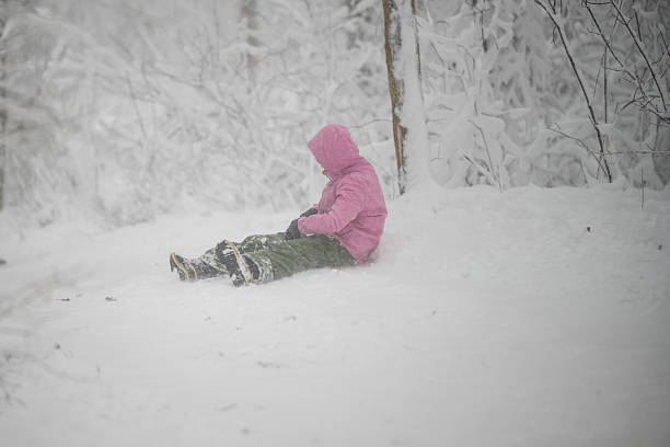 Child wearing a pink coat, green pants, and boots playing in the deep snow of a winter forest. Experiencing cold weather