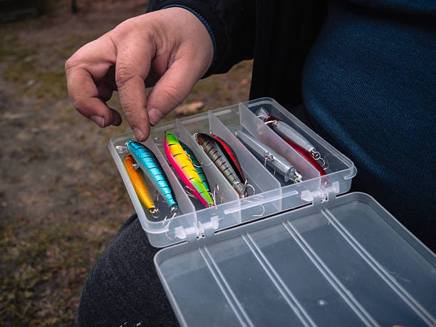 Hand-picking brightly colored lures. The tackle box is open on the lap, and the angler is selecting lures and plastic compartments with bright trim. Get the rods ready.