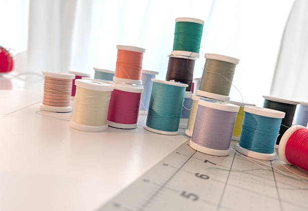 Variety of thread spools in different colors and sizes. A gray pattern cutting board shows a grid of one-inch squares. Artificial lighting in front. Natural light diffused through a window curtain in back.