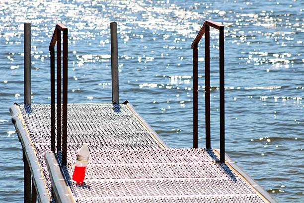 A lake view with a dock and a single red colored drink . The sun is shining brightly on the water and the metal dock.