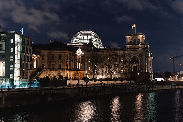Berlin, Germany – January 2, 2026: The Reichstag building with the Bundestag glass dome is illuminated at night and reflected in the River Spree.