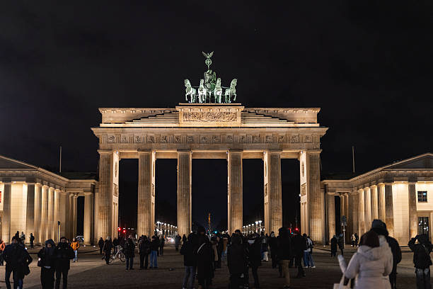 Berlin, Germany – January 2, 2026: People gather near the illuminated Brandenburg Gate in central Berlin during nighttime hours.