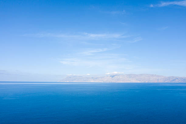 Vast, calm blue water stretches toward a hazy mountain range under a clear sky near Kissamos, Crete. The open expanse and soft light evoke a sense of freedom and tranquility.