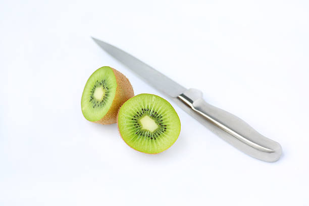 A fresh green kiwi fruit cut in half with a sharp stainless steel knife on a clean white background.