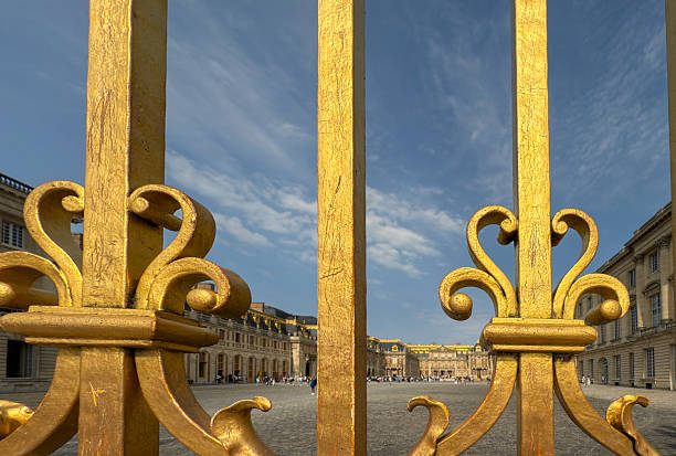 Horizontal close-up photo of decorative bars on the Royal Gate , covered in 23 carat gold leaf over wrought iron, built 2008/2009 at the entrance to the Palace of Versailles. The Palace can be seen in the far distance.