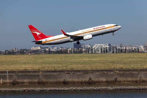 A Qantas Boeing B737-838 plane, registration VH-XZP in Retro Livery, taking off from the third runway of Sydney Kingsford Smith Airport as flight QF161 to Wellington. In the far background are buildings at Brighton Le-Sands on the western shore of Botany Bay. This image was taken from Mill Stream Lookout, Botany Bay on a hot and sunny morning on 9 January 2026.