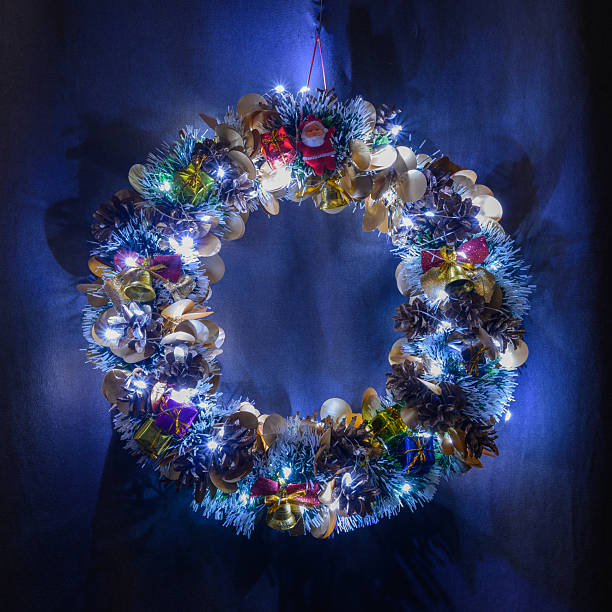 beautiful decorative wreath decorated with cones, golden bells, small presents and a santa figure shines with white led garland lights against a dark blue background