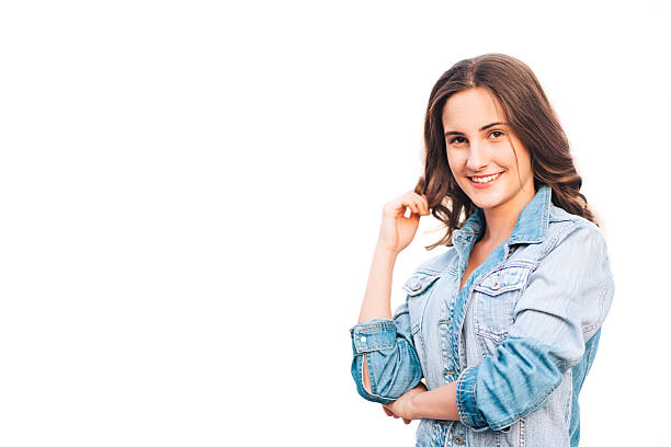 Portrait of a smiling young woman in a denim jacket, playfully touching her hair while looking directly at the camera. The white background highlights her confident posture and friendly expression, creating a bright and approachable visual.
