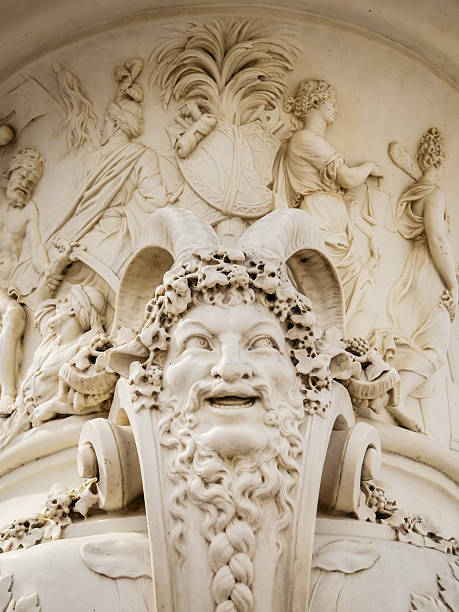 Decorative sculpted mask with classical relief figures on a facade of the Palace in the historic gardens at the Chateau de Versailles near Paris, France.